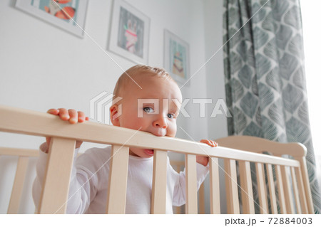 Blond cute little baby biting wooden bed headboard 72884003
