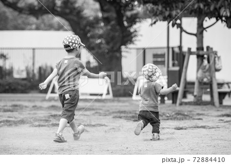 公園で遊ぶ幼い兄弟2人の後ろ姿のモノクロ写真の写真素材