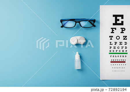 Glasses with Contact Lenses, drops and an Optometrist's Eye Test Chart On a Blue Background. Glasses with Contact Lenses, drops and an Optometrist's Eye Test Chart On a Blue Background. 72892194