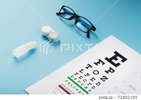 Glasses with Contact Lenses, drops and an Optometrist's Eye Test Chart On a Blue Background. Glasses with Contact Lenses, drops and an Optometrist's Eye Test Chart On a Blue Background. 72892195