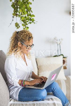 Beautiful woman work and have relax at home with laptop computer - concept of smart work and alternative office - female enjoy technology on the couch and smile - modern lady with connection Beautiful woman work and have relax at home with laptop computer - concept of smart work and alternative office - female enjoy technology on the couch and smile - modern lady with connection 72895687