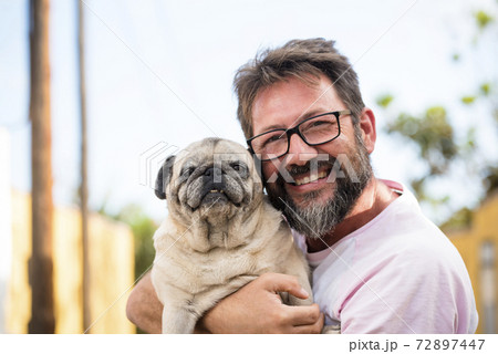 people and dogs love concept - Funny and happy portrait of young handsome adult man and best friend forever together dog pug both looking on camera - outdoor sky and park background people and dogs love concept - Funny and happy portrait of young handsome adult man and best friend forever together dog pug both looking on camera - outdoor sky and park background 72897447
