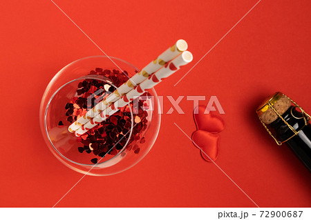 Glass with heart-shaped candy and a bottle of champagne on a red background with space for text. Holiday concept. 72900687