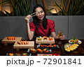 Woman is holding chopsticks with sushi opposite her eye 72901841