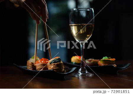 Hand, chopsticks, sushi set and white wine on dark background Hand, chopsticks, sushi set and white wine on dark background 72901851