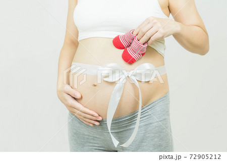 A tummy of a pregnant woman with white ribbon tie bow baby's bootees,Pregnancy health care preparing for baby concept.Motherhood among teenage mother, hugging belly, isolated on gray background A tummy of a pregnant woman with white ribbon tie bow baby's bootees,Pregnancy health care preparing for baby concept.Motherhood among teenage mother, hugging belly, isolated on gray background 72905212