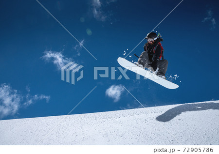 Woman athlete snowboarder in flight after jumping on a snowy slope against a background of a dark blue sky 72905786