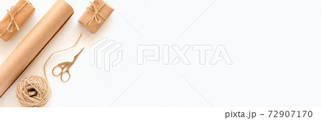 Set of materials for packing holiday gifts. Banner made of kraft paper, jute twine, scissors, boxes on white background. Holiday zero waste and eco-friendry concept. Top view Flat lay Copy space Set of materials for packing holiday gifts. Banner made of kraft paper, jute twine, scissors, boxes on white background. Holiday zero waste and eco-friendry concept. Top view Flat lay Copy space 72907170
