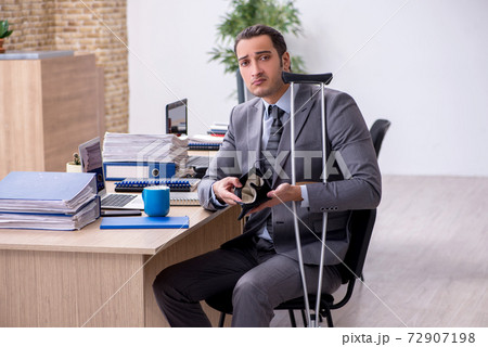 Young leg injured male employee working in the office Young leg injured male employee working in the office 72907198