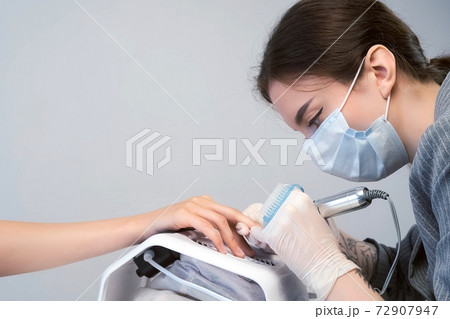 Portrait of woman manicurist in mask cleaning pterygium on nail using apparatus. Portrait of woman manicurist in mask cleaning pterygium on nail using apparatus. 72907947