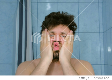 Sleepy shaggy young man with headache in bathroom in morning rubs his face. Sleepy shaggy young man with headache in bathroom in morning rubs his face. 72908122