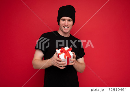 Shot of handsome happy young man isolated over red background wall wearing black hat and black t Shot of handsome happy young man isolated over red background wall wearing black hat and black t 72910464
