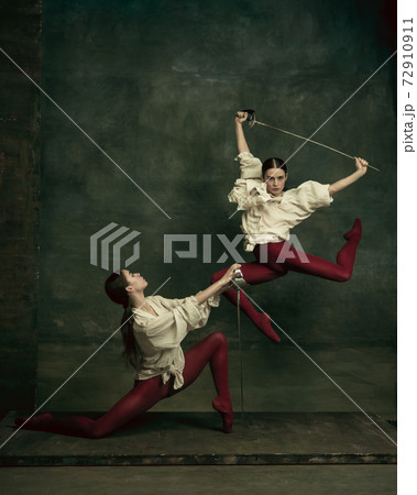 Two young female ballet dancers like duelists with swords. Ballet and contemporary choreography concept. Creative art photo. Two young female ballet dancers like duelists with swords. Ballet and contemporary choreography concept. Creative art photo. 72910911