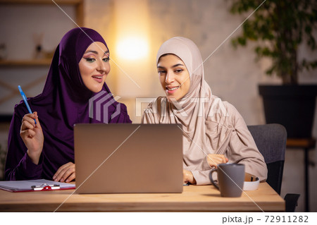 Happy two muslim women at home during lesson, studying near computer, online education Happy two muslim women at home during lesson, studying near computer, online education 72911282