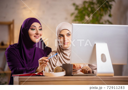 Happy two muslim women at home during lesson, studying near computer, online education Happy two muslim women at home during lesson, studying near computer, online education 72911283