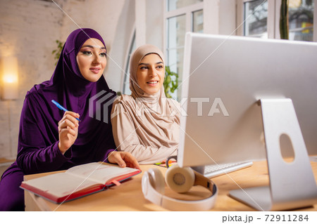 Happy two muslim women at home during lesson, studying near computer, online education 72911284