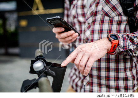 Male hands modern electric scooter turns on and tunes. Caucasian man dressed stylishly casual uses cell phone to control kick scooter, close-up no face. Personal electric transport in city Male hands modern electric scooter turns on and tunes. Caucasian man dressed stylishly casual uses cell phone to control kick scooter, close-up no face. Personal electric transport in city 72911299