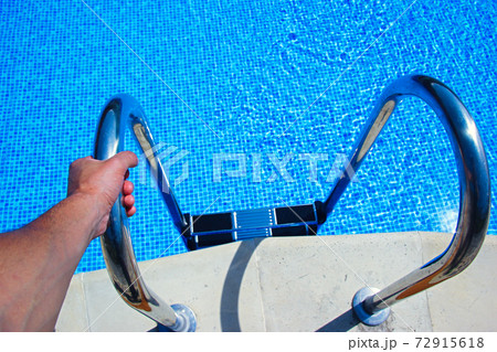 Stairs to the pool filled with clean water. Hand holds the handrail. 72915618
