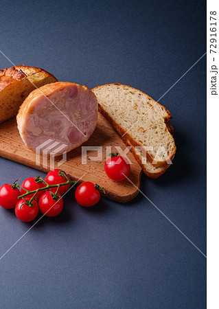 Turkey ham meat, fresh cherry tomatoes branch and loaf sliced bread on wooden cutting board, blue minimal background, angle view, copy space Turkey ham meat, fresh cherry tomatoes branch and loaf sliced bread on wooden cutting board, blue minimal background, angle view, copy space 72916178