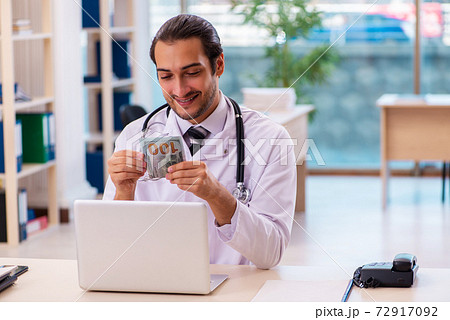 Young male medic holding banknote in the clinic Young male medic holding banknote in the clinic 72917092