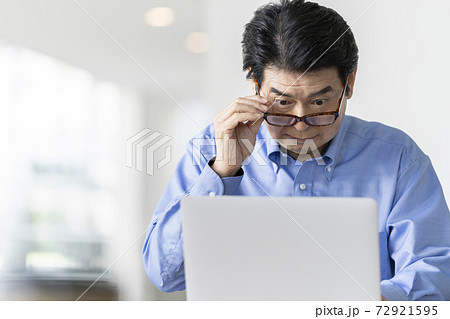 老眼鏡をかけてノートパソコンの画面を見るシニア男性 72921595
