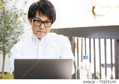 【ワーケーション】ホテルのテラスで集中して仕事をする男性 72925144