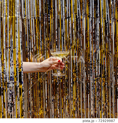 Hand holds a glass of champagne on the background of shiny metallic curtain 72929987