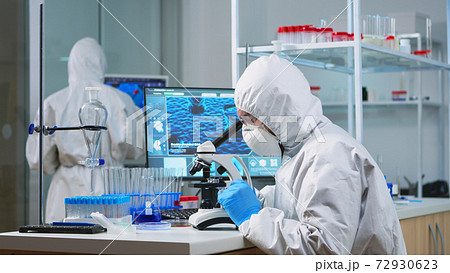 Chemist researcher in coverall looking at bacteria sample from glass Chemist researcher in coverall looking at bacteria sample from glass 72930623