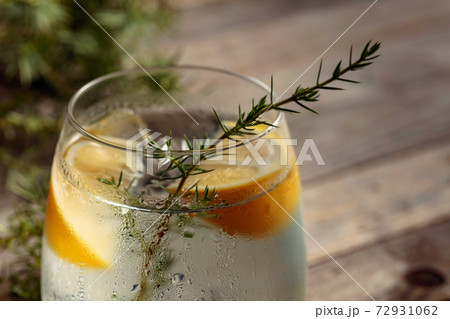 Alcohol drink (gin tonic cocktail) with lemon, juniper branch, and ice on rustic wooden table. 72931062