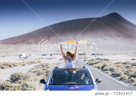Happiness and travel lifestyle concept with beautiful woman outside a convertible blue car enjoy the freedom and have fun on the road with her female friends driving the vehicle - friends and 72931457