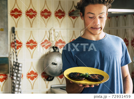 Young teenager with burned too cooked hamgurger with funny expression in the kitchen 72931459