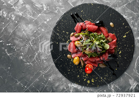 Beef carpaccio with arugula on a black plate, traditional Italian cuisine. Dark key, copy space, Beef carpaccio with arugula on a black plate, traditional Italian cuisine. Dark key, copy space, 72937921
