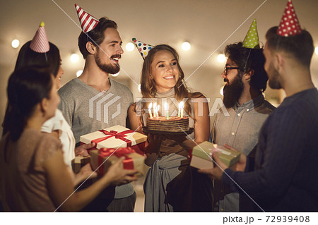 Happy young woman holding her birthday cake and thanking friends for party and presents 72939408