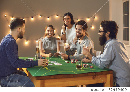 Cheerful company of male and female friends sitting at a poker table and enjoying the evening. Cheerful company of male and female friends sitting at a poker table and enjoying the evening. 72939409