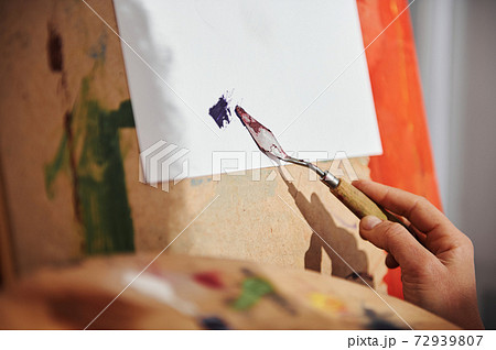 Closeup of hand of the artist's woman smears with a palette knife on a white canvas. Focus on palette knife 72939807