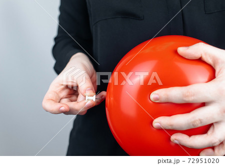 Conceptual photography. The woman holds a red ball near his belly, which symbolizes bloating and flatulence. Then she brings a needle to it to burst the balloon and thus get rid of the problem. Conceptual photography. The woman holds a red ball near his belly, which symbolizes bloating and flatulence. Then she brings a needle to it to burst the balloon and thus get rid of the problem. 72951020