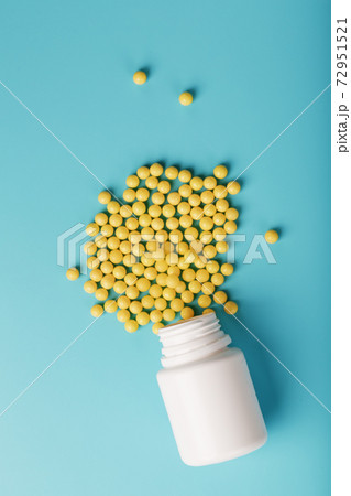 Yellow vitamin C capsules spilled out of a white jar against a blue background. Yellow vitamin C capsules spilled out of a white jar against a blue background. 72951521