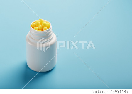 Vitamins of yellow color in the form of round dragees in a white jar on a blue background. Vitamins of yellow color in the form of round dragees in a white jar on a blue background. 72951547