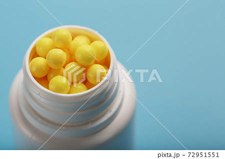 Vitamins of yellow color in the form of round dragees in a white jar on a blue background. 72951551