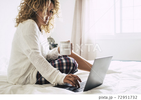 Young adult woman working at home in the bedroom during morning breakfast work activity - quarantine for coronavirus health emergency - happy female with computer laptop and coffe cup - bright white Young adult woman working at home in the bedroom during morning breakfast work activity - quarantine for coronavirus health emergency - happy female with computer laptop and coffe cup - bright white 72951732