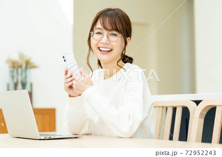 リビングでノートパソコンを使いながら電話をする女性の写真素材