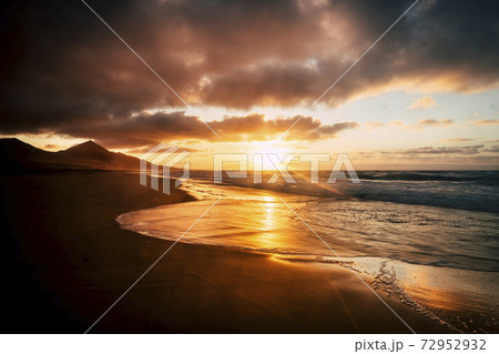 Wonderful timeless sunset at the beach with dramatic clouds and waves - mountains in background and wild scenic place - golden and fire colors in a beauty of nature 72952932