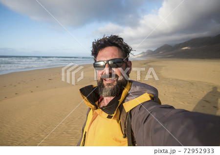Happy wild lifestyle people concept with cheerful handsome adult man in wild beach with mopuntains in background - alternative summer vacation with adventure taste - caucasian male selfie 72952933