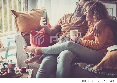 Video conference call and connection with modern friends online concept for adult cheerful beautiful couple at home using internet technology sitting on the sofa - people together and communication 72953104