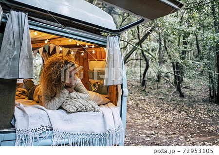 Happy free beautiful woman lay down and relax inside her blue van vehicle parked in the forest - people enjoying alternative travel and vacation or life options - female enjoying the camper van 72953105