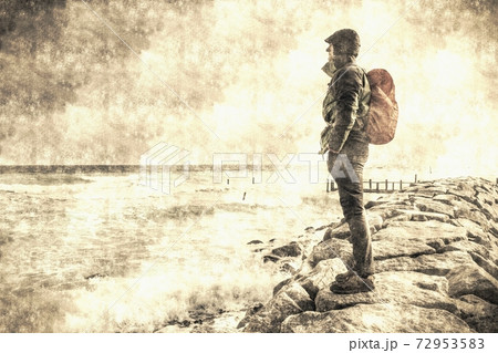 Young man with backpack standing on beach and looking to horizon of ocean. 72953583
