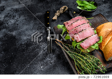 Baguette Tuna steak sandwich with arugula on a cutting board. Black background. Top view. Copy space 72961669