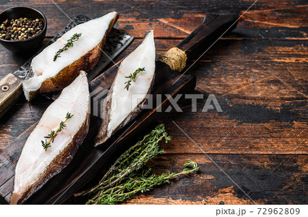 Raw fresh halibut fish steak on a wooden cutiing board. Black background. Top view. Copy space Raw fresh halibut fish steak on a wooden cutiing board. Black background. Top view. Copy space 72962809
