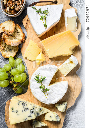 Assorted cheeses on a wooden cutting Board. Camembert, brie, Parmesan and blue cheese with grapes and walnuts. White background. Top view 72962974