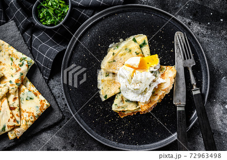 Plate of pancake stuffed with spinach and eggs. Black background. Top view Plate of pancake stuffed with spinach and eggs. Black background. Top view 72963498
